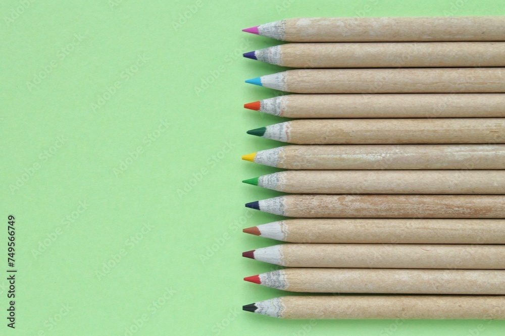 Obraz premium Multi colored pencils isolated on green background. Back to school concept. Sketching and drawing hobby. Stationery supply store. Education process. Top view. Minimal style composition