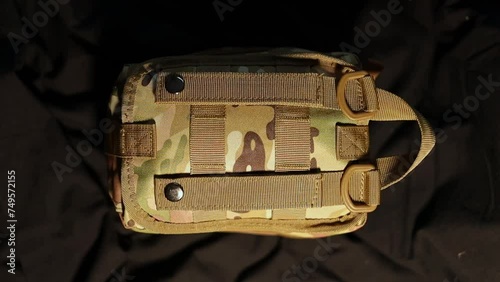 Military tactical first aid kit. Tactical military first aid kit with red cross chevron close-up. Military first aid kit in camouflage color on a dark background. First aid for wounds and injuries.  photo