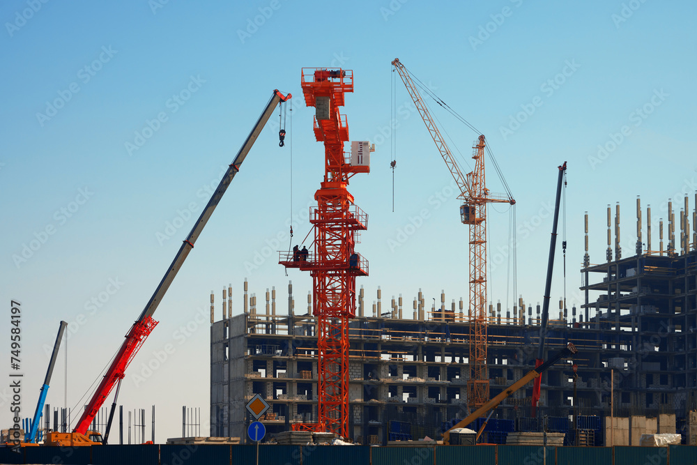 Panoramic view of a construction site with a multi-storey building under construction, construction cranes, truck cranes and building materials in the northern region.