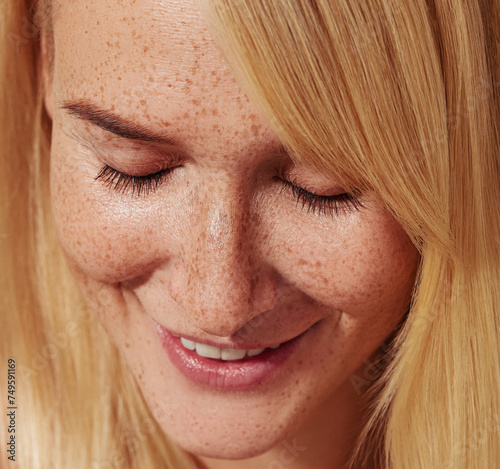 Close-up of smiling blond female with freckles looking down. Highly detailed close-up shot of a young female with smooth freckled skin.