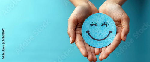 smiling blue paper face with cute eyelashes held by hands on turquoise background, free space for text, world health day  concept  photo