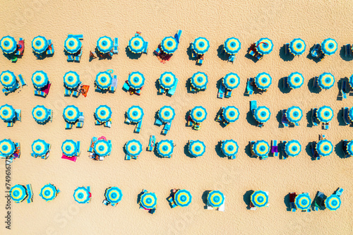 Aerial view of colorful blue umbrellas on sandy beach on summer sunny day in Sardinia, Italy. Tropical landscape. Travel and vacation background. Top down view from drone. Tropical pattern. Seaside