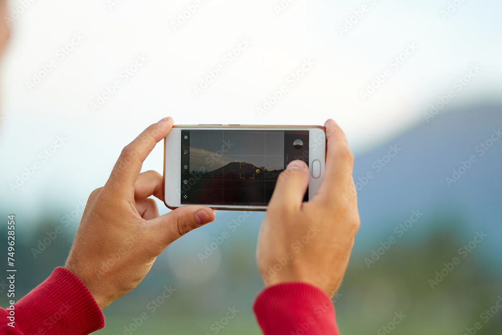 A young man stands on the side of the road near a rice paddy and takes a picture with his phone of Mount Agung on the popular tourist island of Bali. A young man stands on the side of the road near a rice paddy and takes a picture with his phone of Mount Agung on the popular tourist island of Bali.
