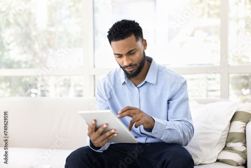 Serious African entrepreneur man using tablet for job communication at home, typing on digital gadget, working with online app, Internet ecommerce service, browsing social media network