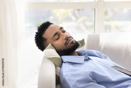 Serene sleepy attractive young African business man relaxing at work break  sleeping on sofa at daytime  taking nap  enjoying peace  relaxation  recreation  feeling tired  exhausted