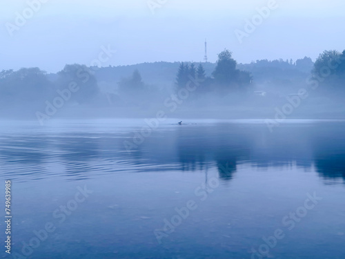 Morning fog on the lake in the early misty morning. The trees are reflected in the water.