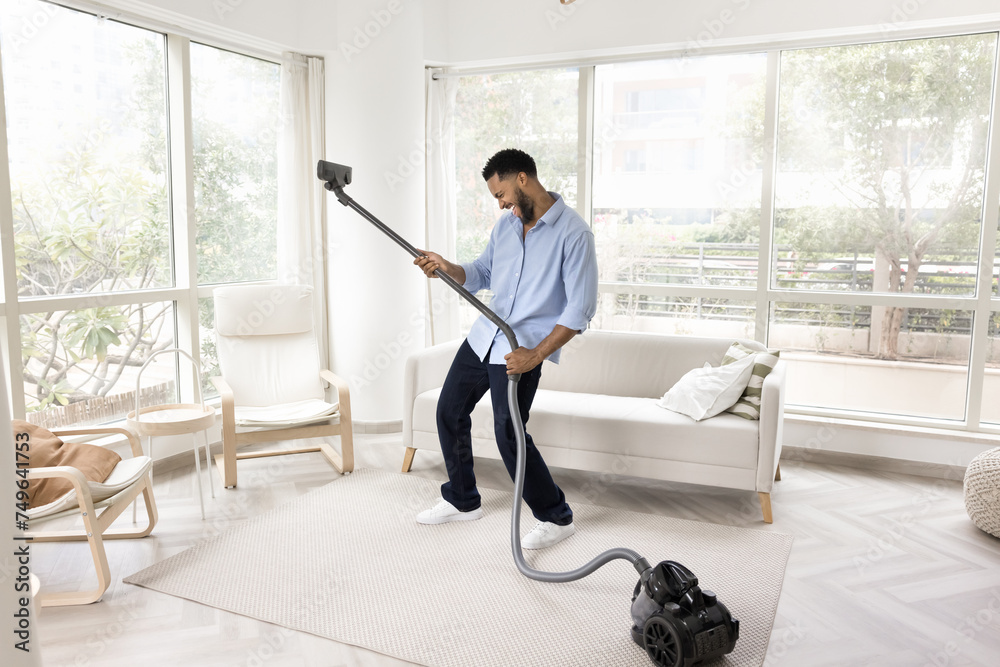 custom made wallpaper toronto digitalCheerful Black homeowner guy having fun while tidying up at home, vacuuming carpeted floor in living room, dancing to music, singing song, imitating guitar playing with hoover