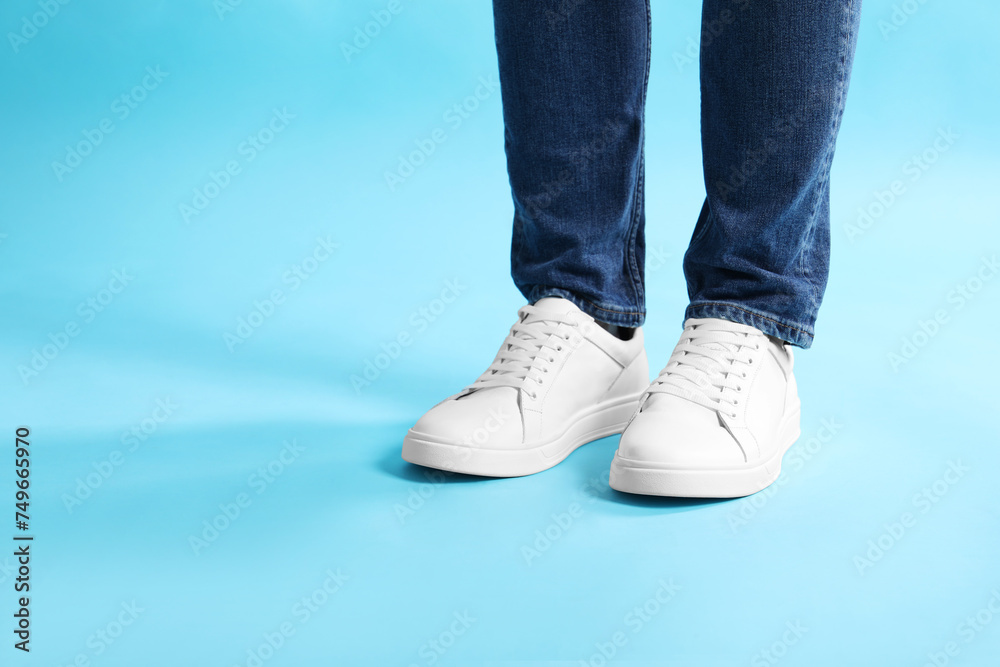 Man wearing stylish white sneakers on light blue background, closeup