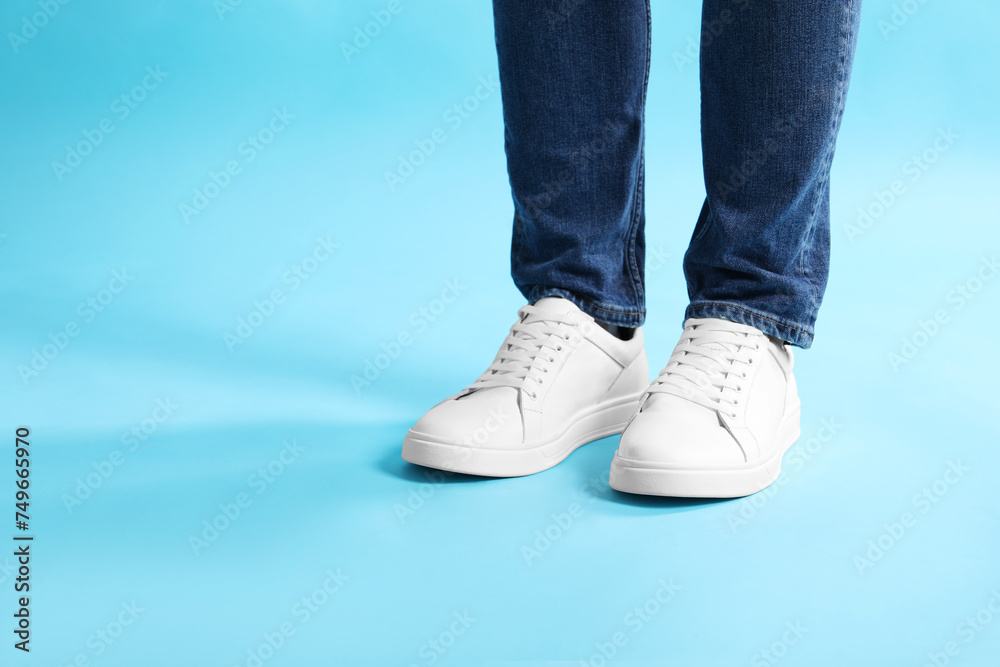 Man wearing stylish white sneakers on light blue background, closeup Man wearing stylish white sneakers on light blue background, closeup