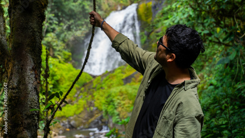 Slika na platnu Hombre joven latino cogiendo con su mano una rama de un árbol en el bosque