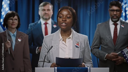 Medium shot of young African American female politician campaigning for presidential or governor nomination from US Republican Party addressing voters at tribune, ending speech, thanking and waving photo