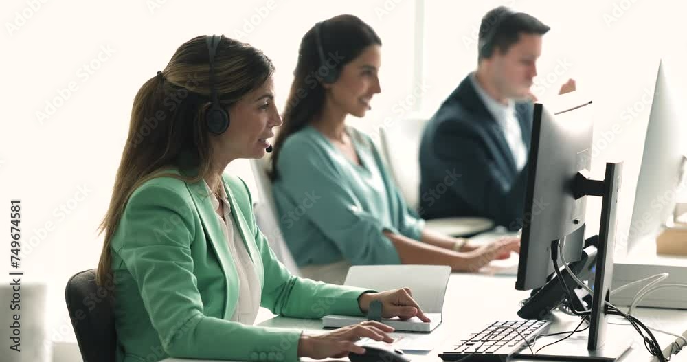 Smiling Hispanic woman call center agent, telemarketer in headset talking, consulting on-line client using PC sit at shared desk with workmates, working in customer support helpdesk services office