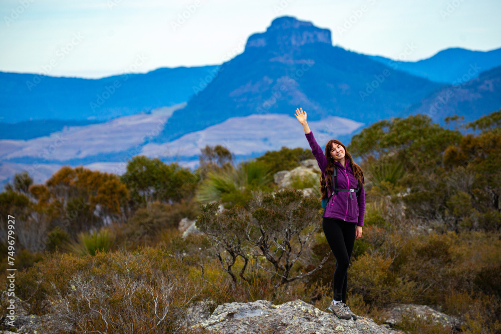 backpacker girl celebrating successful hike to the summit of mount maroon; rock scrambling in mount barney national park, queensland, australia