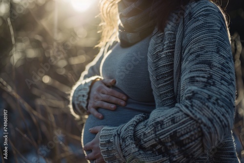 A close up of a pregnant woman cradling her belly with gentle hands against a backdrop of soft natural light embodying the beauty of motherhood