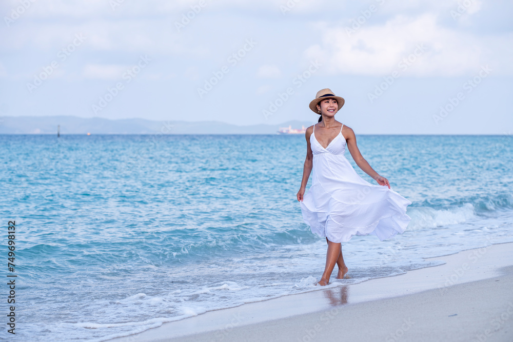 Happy sexy Asian traveller woman wear white beach dress and hat show enjoys on tropical beach vacation in summer holidays Happy sexy Asian traveller woman wear white beach dress and hat show enjoys on tropical beach vacation in summer holidays