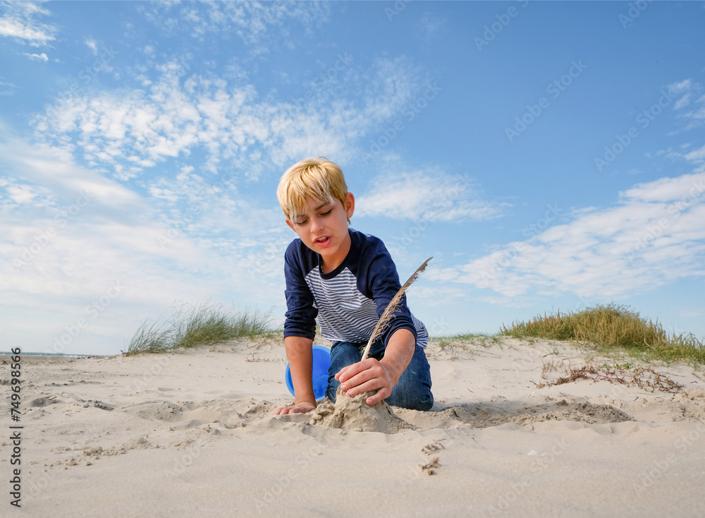 Little blond boy at the beach building a sandcastle with sand and a bucket Little blond boy at the beach building a sandcastle with sand and a bucket