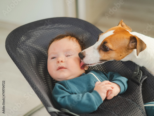 Foto A dog licks the face of a cute three-month-old boy dressed in blue overalls in a baby lounger