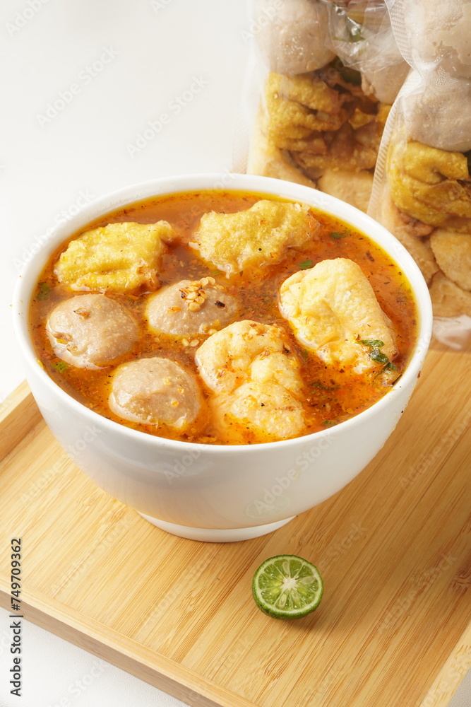 Savor a bowl of Cuankie meatball soup with round meatballs, tofu, fried wontons, and savory spicy broth, elegantly presented in a white bowl on a wooden base against a white background. Savor a bowl of Cuankie meatball soup with round meatballs, tofu, fried wontons, and savory spicy broth, elegantly presented in a white bowl on a wooden base against a white background.