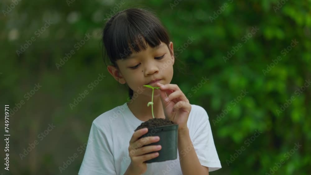 A Thai Asian kid girl, aged 8 to 10 years, has a cute face and a bright smile. She held a pot of seedlings in her hand. trees are going to be planted To care for a sustainable world, Earth Day concept