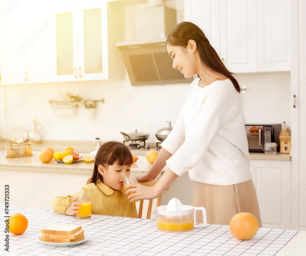 Asian mother drinking freshly squeezed orange juice with her daughter in the kitchen