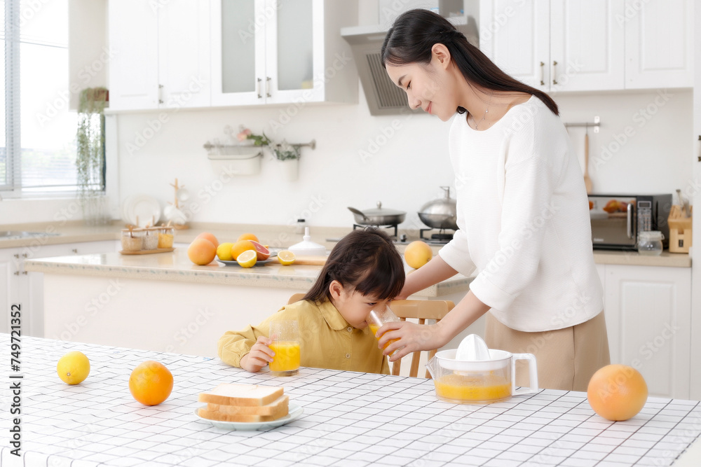 Asian mother drinking freshly squeezed orange juice with her daughter in the kitchen