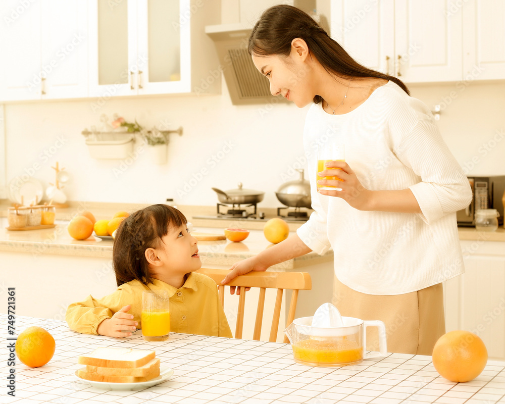 Asian mother drinking freshly squeezed orange juice with her daughter in the kitchen