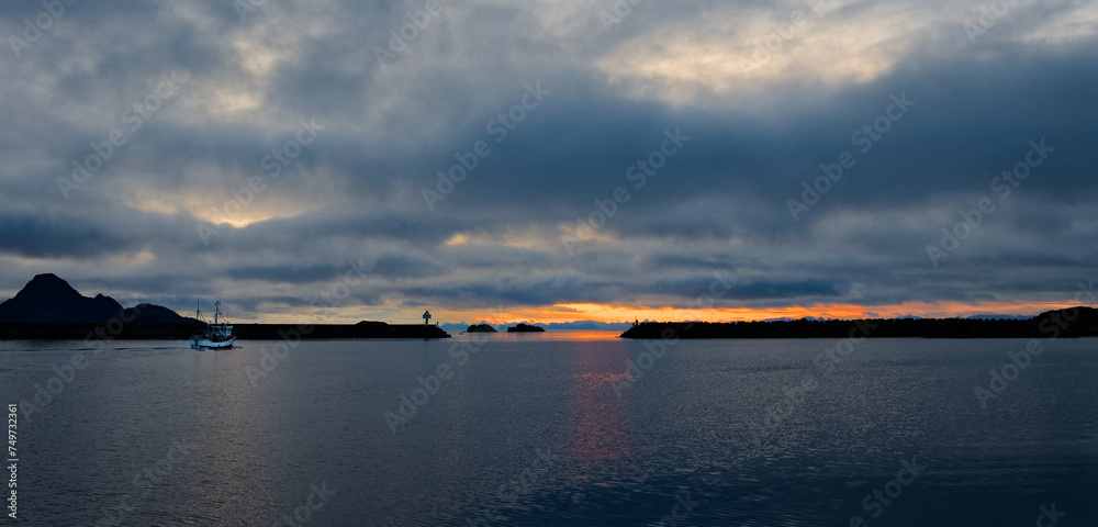 Fishing boat leave the bay and harbour towards the open sea in cloudy morning at sunrise. Lofoten Islands, Northern Norway.
