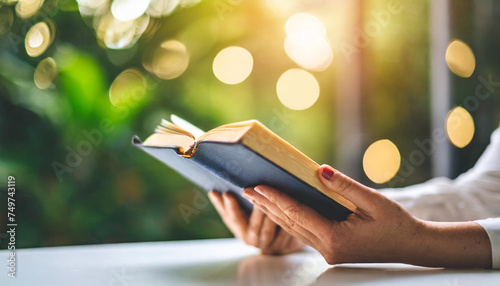 woman's hands cradle Bible on white table, bathed in bright backlight