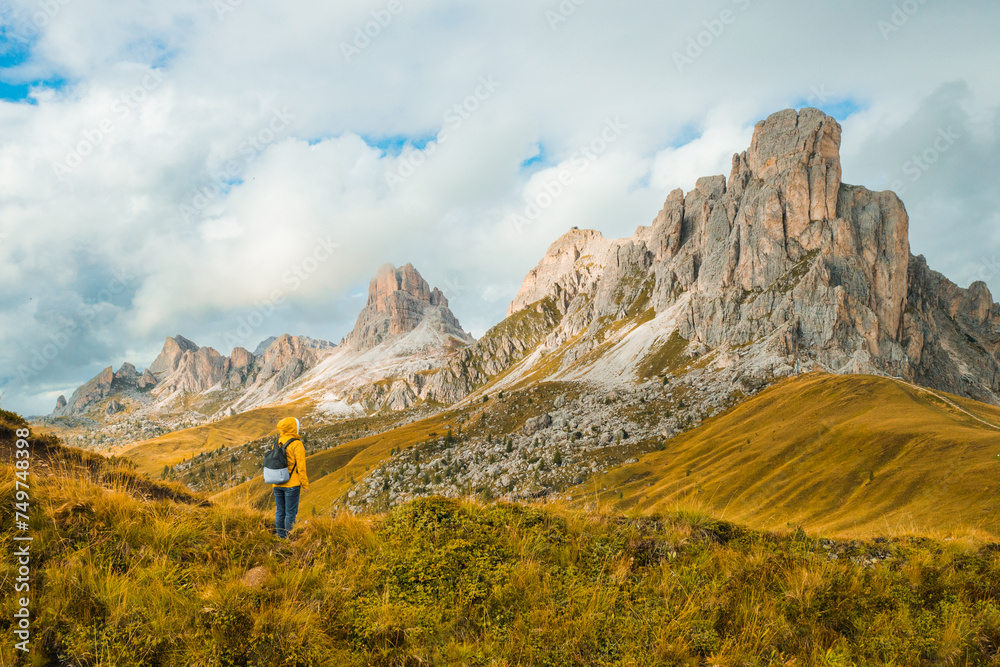 Tourist in yellow jacket and backpack enjoying the famous Giau Pass and Dolomites Alps