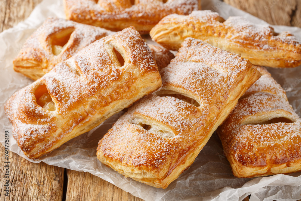 Delicious apple puffs with powdered sugar close-up on paper on a wooden table. Horizontal