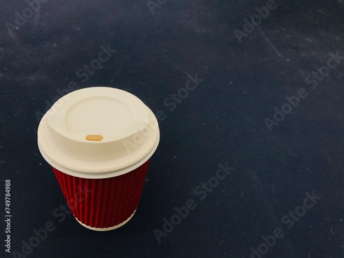 A red paper coffee cup with a white plastic lid sits on a plain blue background which has the copy space on the right side of frame