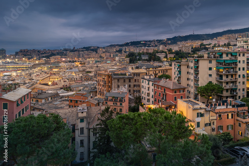 Panoramic cityscape with illuminated residential district on hillside under cloudy sky, Genoa, Italy