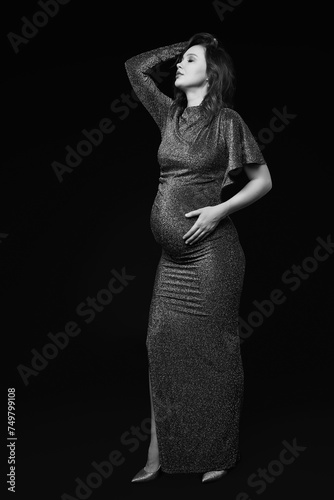 Black and white portrait of pregnant female in grey sequin dress with hands near pregnant belly.