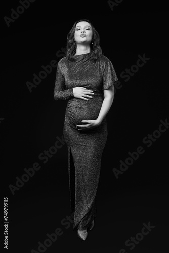Black and white portrait of pregnant female in sequin dress with hands near pregnant belly.  Lips in an air kiss.