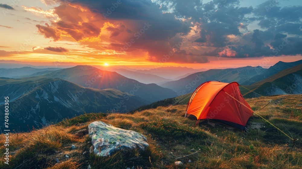 Glowing orange tent in the mountains under dramatic evening sky. Red sunset and mountains in the background. Summer landscape. Panorama