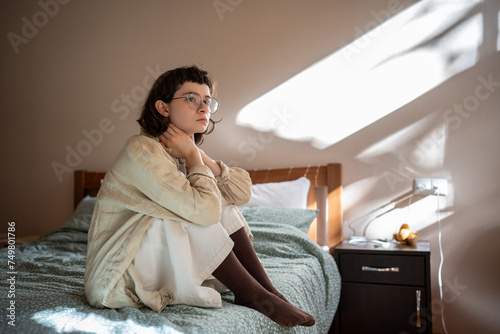 Melancholic lonely teen girl sits on bed, sadly looking at window, feeling anxiety depression. Frustrated worried teenager thinking about school bullying. Adolescence, puberty, awkward age troubles.