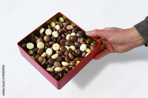 Hand offers square cookie tin with chocolate cookies. Studio shot subject is made isolated on white background