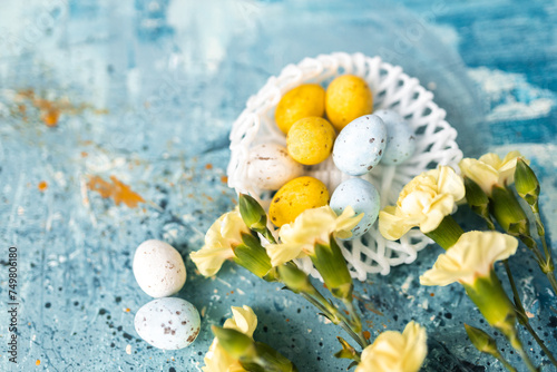 Yellow beautiful flowers and blue, yellow colored easter eggs in wicker basket on a blue picturesque oil painting background close up. spring Mockups. Layout. Easter pastel contemporary background