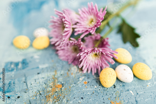 Pink flowers and yellow and white colored easter eggs on a blue picturesque oil painting background close up. Spring Mockups with pink Gerbers. Layout. Easter pastel background