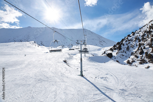 Chunkurchak ski resort in Kyrgyzstan. Empty ski lift seats. Mountain slope at sunny winter day, blue sky. Active recreation skiing and snowboarding. Support pillar, Cable car ride. © Sea_Inside_Soul