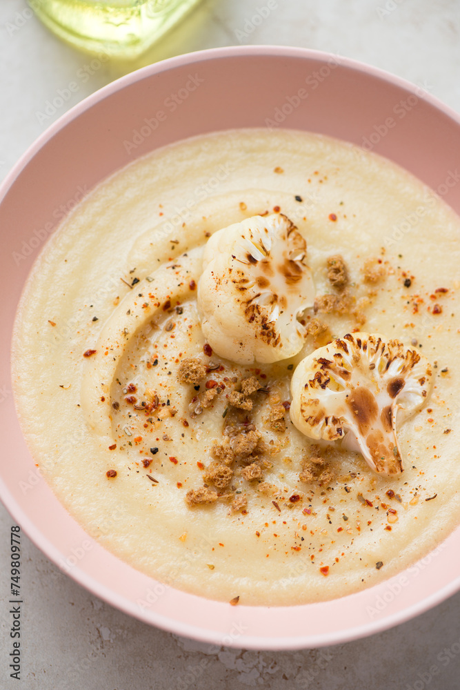 Cream-soup made of roasted cauliflower cabbage and served in a roseate bowl, vertical shot, middle close-up, selective focus