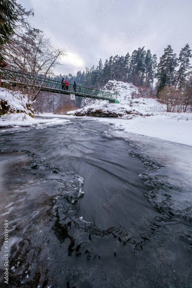 Half-frozen Hornad river with rapids in winter at sunset Slovak Paradise. An iron bridge over a frozen river. Discovering the beauty of the winter landscape.
