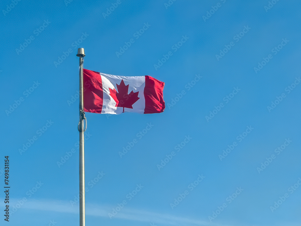 A dynamic movement of a waving Canadian flag, captured in a still image against the backdrop of a clear blue sky during daylight. A dynamic movement of a waving Canadian flag, captured in a still image against the backdrop of a clear blue sky during daylight.