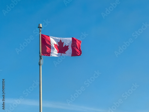 A dynamic movement of a waving Canadian flag, captured in a still image against the backdrop of a clear blue sky during daylight.