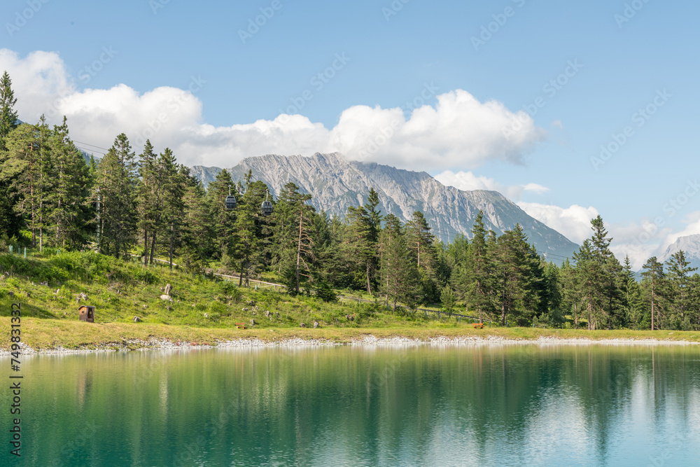 Beautiful summer view of a small alpine lake in the alpine mountains in Imst, Tirol. Water reservoir in beautiful Imst, surrounded by alpine pine trees. Wild flowers and grass. Tranquil scene.