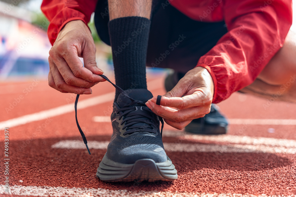 Close up male runner tied the rope, prepare jogging shoes on running track background, outdoor workout concept, drink clear mineral water after jogging. Generation z lifestyle.	