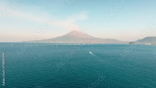 晴れた日の鹿児島湾の青い海と噴煙を上げる桜島の火山に向かって進む漁船　空撮