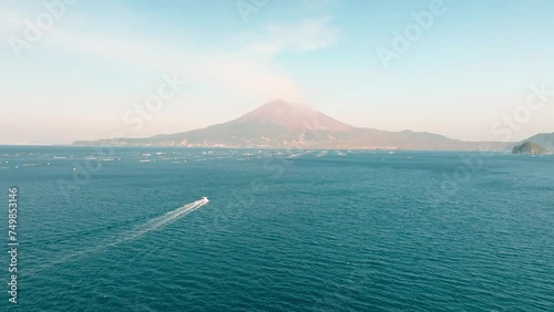 晴れた日の鹿児島湾の青い海と噴煙を上げる桜島の火山に向かって進む漁船　空撮