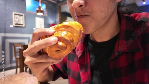 Slow motion video of an asian man is eating butter croissant bread. Concept for unhealthy food, fat loss, weight loss, bad diet, diabetes, cholesterol, insulin resistance, and metabolic syndrome.