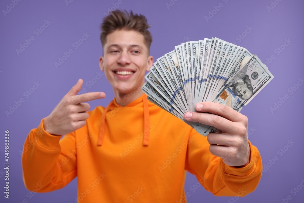Happy man pointing at money on purple background, selective focus Happy man pointing at money on purple background, selective focus